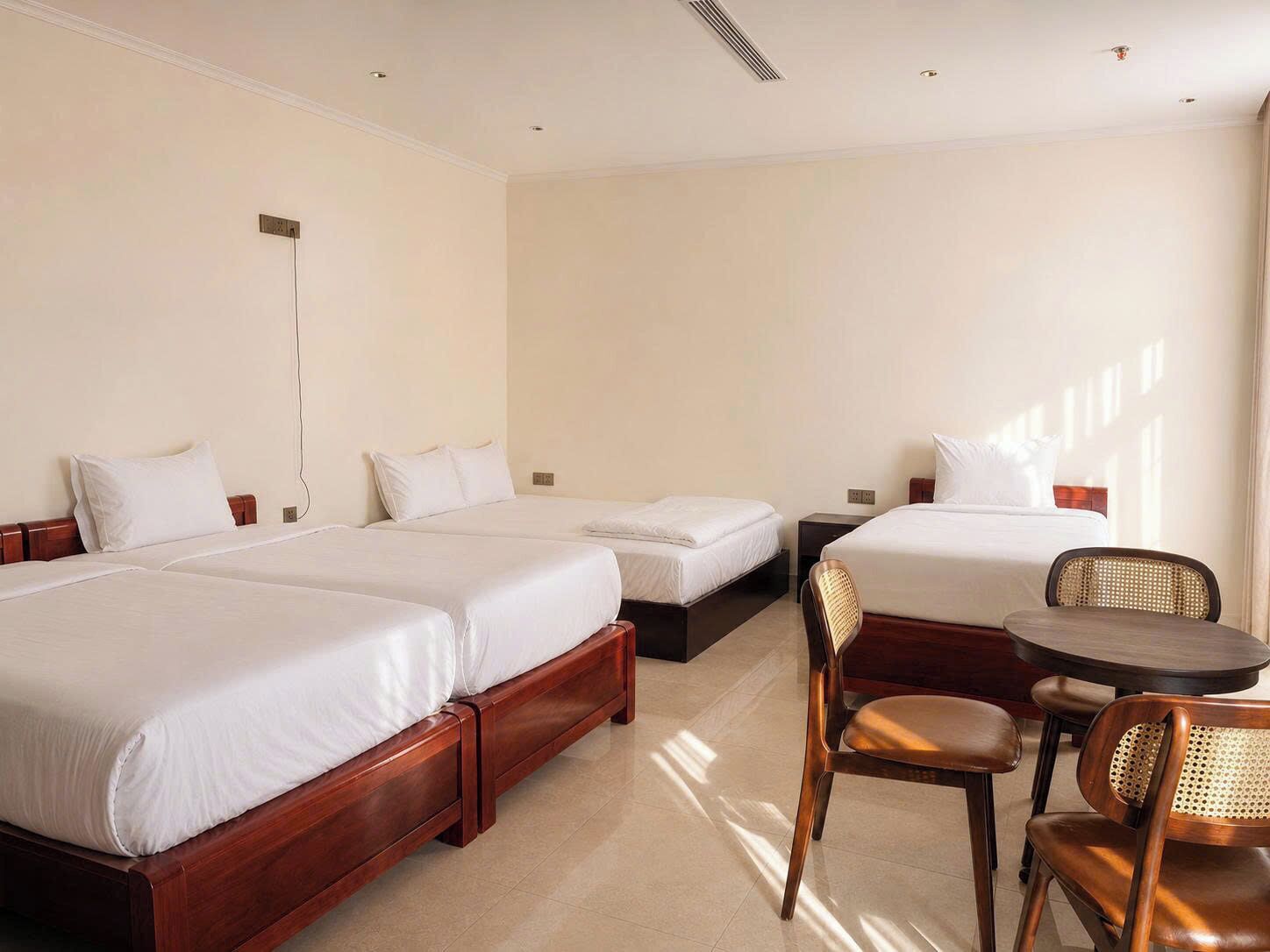 A hotel room with three beds, a dining table, and chairs.