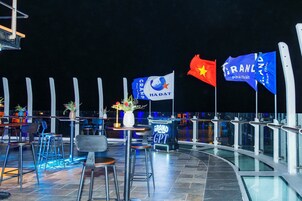 Un área de estar al aire libre con mesas y sillas, banderas y un letrero que dice 'GRAND PHAN THIET'.