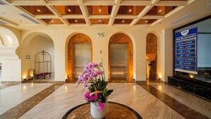 Een receptiehal met een marmeren vloer, een bloemstuk en een bord met daarop de faciliteiten van het hotel.