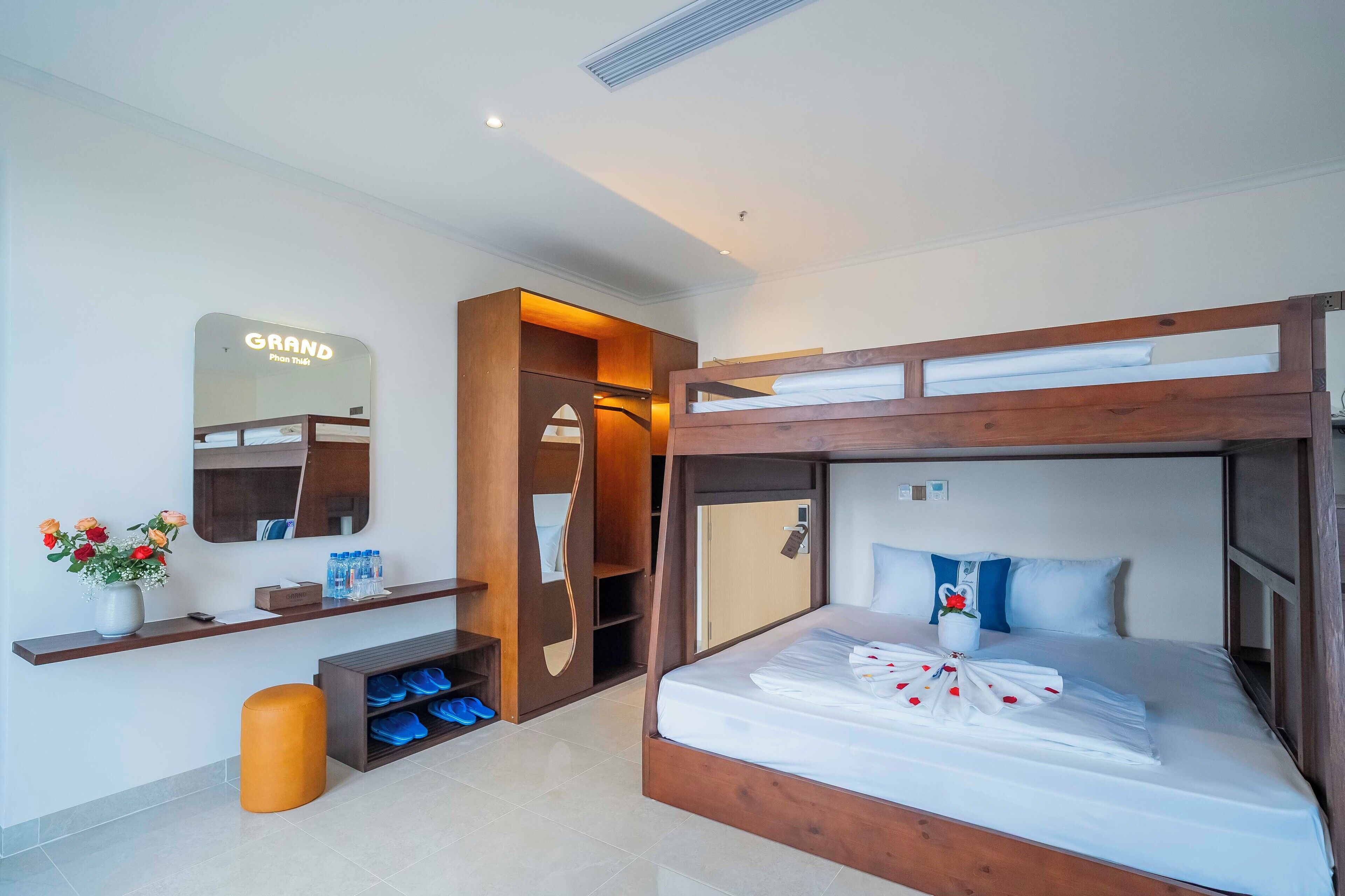 Una habitación de hotel moderna con una litera, un tocador con espejo, un zapatero y una pequeña zona de estar.