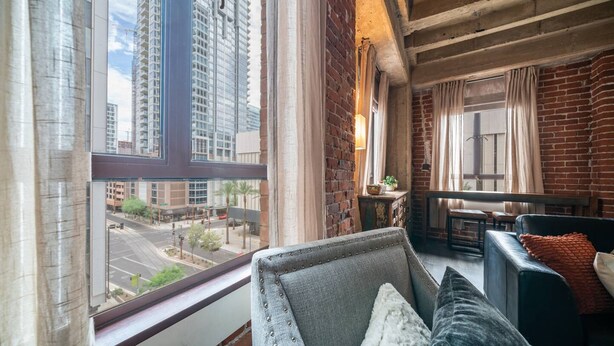 A modern living room with a view of a cityscape, featuring a sofa, a small table, and a window with curtains. - Luxury Downtown Phoenix Loft - Pool Gym Laundry (Phoenix)