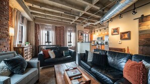 A cozy living room with brick walls, a fireplace, and a kitchen area in the background. - Luxury Downtown Phoenix Loft - Pool Gym Laundry (Phoenix)
