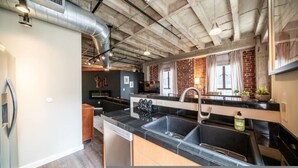 A modern kitchen with a black countertop, stainless steel sink, and a large window with curtains. - Luxury Downtown Phoenix Loft - Pool Gym Laundry (Phoenix)