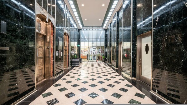 Moderni hotellin aula, jossa on ruutukuviollinen lattia, lasiovet ja marmoriseinät.