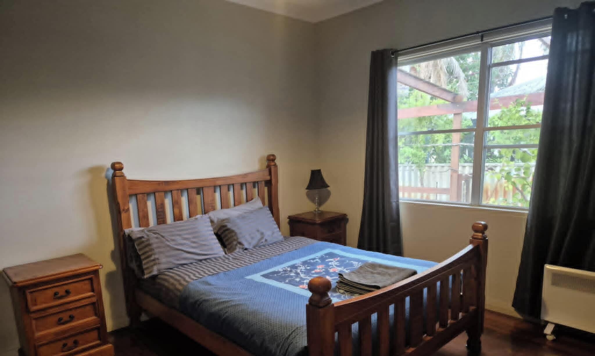 Un dormitorio con una cama de madera, una mesita de noche, un aparador y una ventana con cortinas.