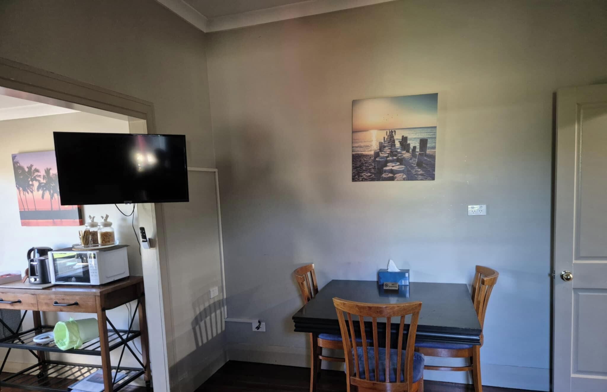 Een eethoek met een tafel en stoelen, een televisie op een standaard, een magnetron en een koffiezetapparaat.
