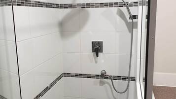 A glass-enclosed shower with white tiles and black mosaic borders, a handheld showerhead, and a wall-mounted faucet.