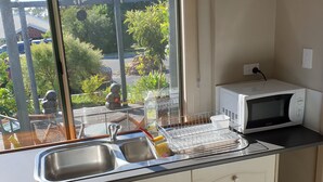 A kitchen with a window view, a sink, a microwave, and a dish rack. - Bunbury's Most Convenient Location (Carey Park)