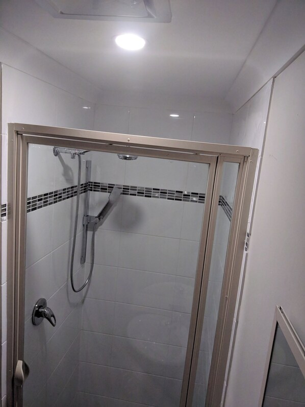 Une douche fermée par des parois en verre, dotée d’un pommeau de douche à main et d’un robinet mural.