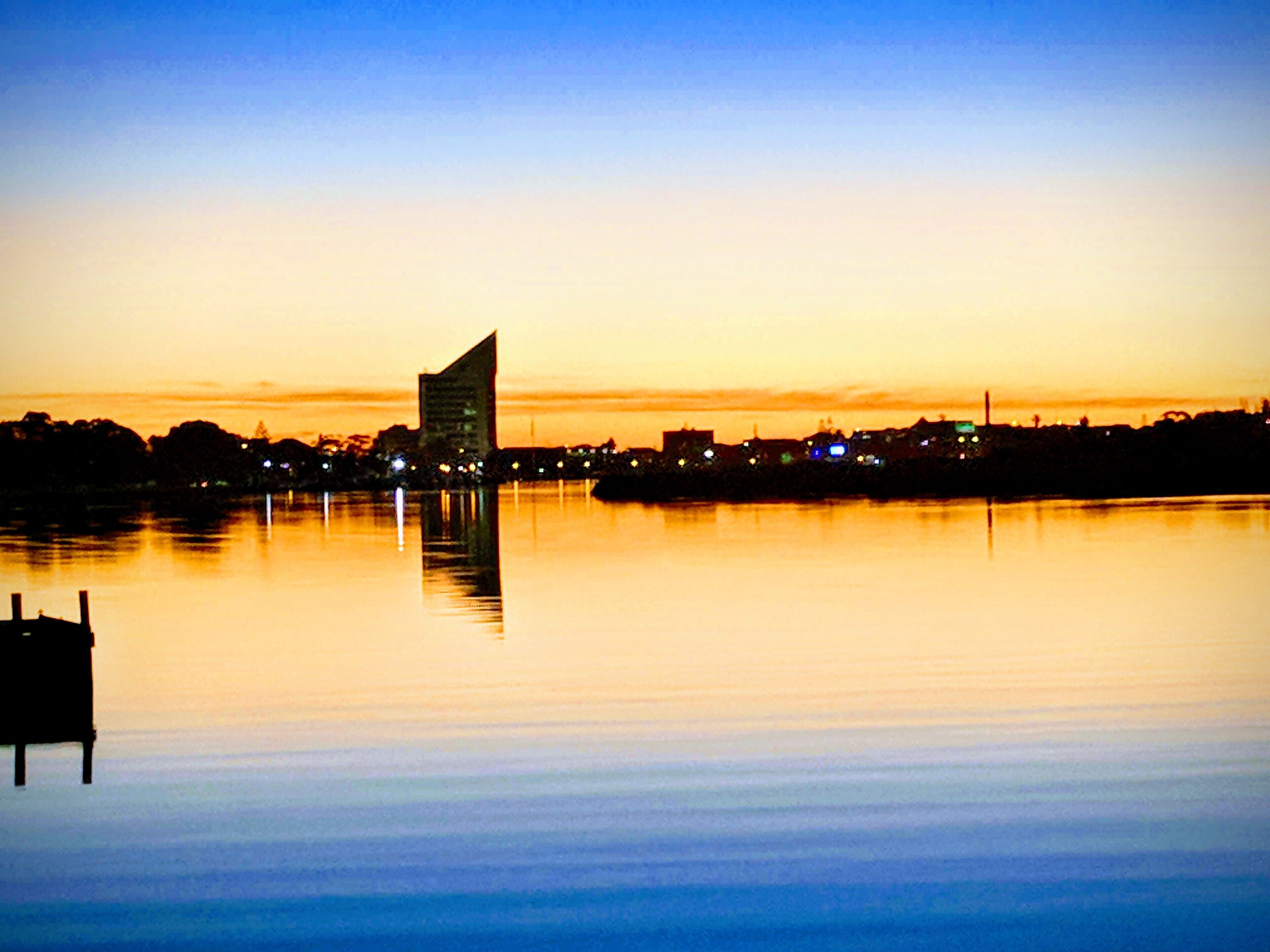 A calm water body reflecting a city skyline with a prominent building at the center.
