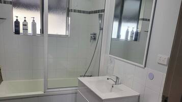 Badeværelse med badekar, håndvask, toilet og bruser. Toiletartikler er anbragt på væggen.