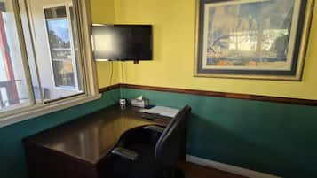 Una habitación con escritorio, silla, ventana y un cuadro en la pared.