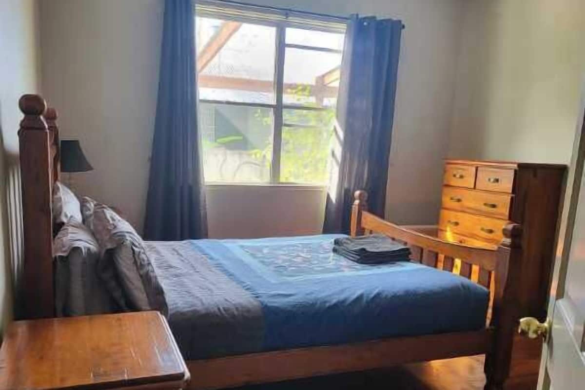A bedroom with a wooden bed, a nightstand, a dresser, and a window with curtains.
