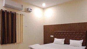 A bedroom with a bed, a ceiling fan, an air conditioning unit, and curtains. - The Krishna Inn (Varanasi)