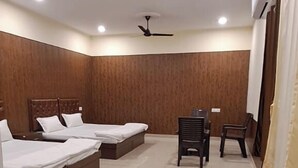 A hotel room with two beds, a ceiling fan, and a small table with chairs. - The Krishna Inn (Varanasi)