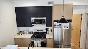 A modern kitchen with black cabinets, stainless steel appliances, and a wooden door.
