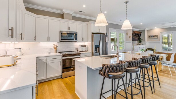A modern kitchen with white cabinetry, stainless steel appliances, and a central island with bar stools. - New Elevated Home | Pool | 6-Seater Golf Cart (Oak Island)