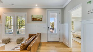 A spacious living area with a wooden bench, a door leading to a bedroom, and a view through the window. - New Elevated Home | Pool | 6-Seater Golf Cart (Oak Island)