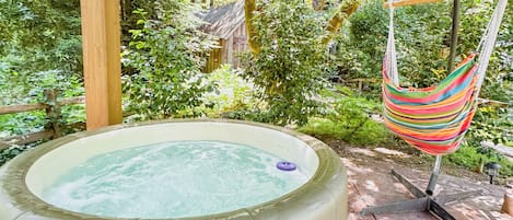 A hot tub under a wooden pergola surrounded by lush greenery.
