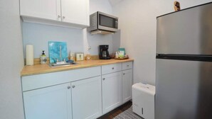 Cocina compacta con armarios blancos, microondas, cafetera y refrigerador.