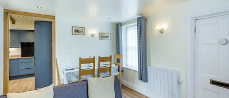 A room with a sofa, a dining table with chairs, a kitchen area, and a white door.