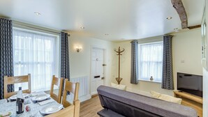 A well-lit room with a dining table set for two, a sofa, a coat rack, and a television.