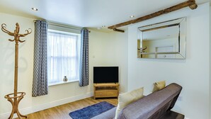 A living room with a sofa, a flat-screen TV, a wooden coffee table, a blue rug, a coat stand, and a large mirror.