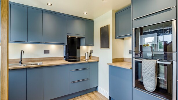 A modern kitchen with grey cabinets, a stainless steel sink, and a built-in oven.