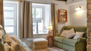 A cozy living room with a green sofa set, a small side table with a lamp, and a window with curtains. - 4 bedroom accommodation in Filey (Filey)