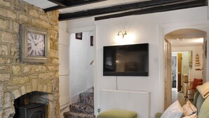 A cozy living room with a stone fireplace, a flat-screen TV mounted on the wall, a green ottoman, and a patterned sofa. - 4 bedroom accommodation in Filey (Filey)