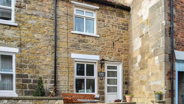 A stone building with a 'Squirrel Cottage' sign, a bench, and a potted plant. - 4 bedroom accommodation in Filey (Filey)