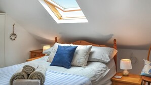 A bedroom with a skylight, a bed with striped bedding, and a bedside table with a lamp. - 4 bedroom accommodation in Filey (Filey)