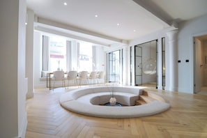 A modern interior with a circular seating area, a dining table with chairs, and a glass partition.