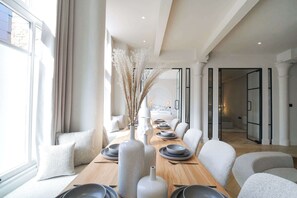 A modern dining area with a long table, white chairs, and a vase with dried plants.