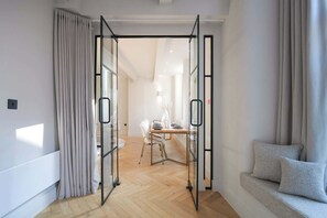 An open door leading to a dining area with a table and chairs, a sofa, and a window with curtains.