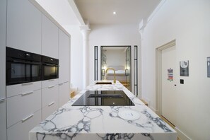 Cozinha moderna com bancada de mármore, fornos embutidos e torneira dourada.