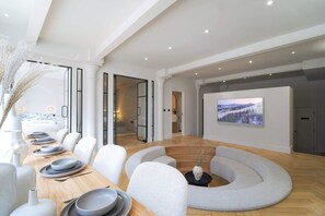 A modern interior with a long dining table, white chairs, a circular seating area, and a large framed picture on the wall. - Blanco | The Heim (Greater Manchester)
