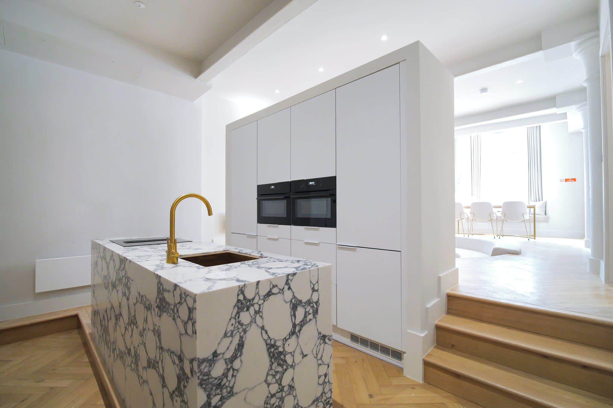 A modern kitchen with white cabinetry, a marble island, and a built-in oven.
