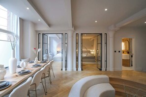 A spacious dining area with a long table, chairs, and a view into a bedroom.