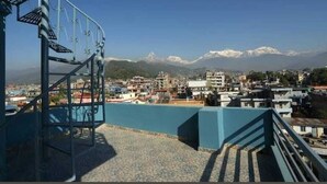 Uma escadaria leva a um terraço com vista para uma cidade, com montanhas ao fundo.