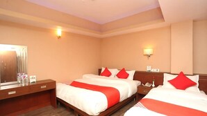 Quarto de hotel com duas camas, uma cômoda de madeira, um espelho e duas luminárias fixadas na parede.