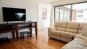 Una sala de estar moderna con un televisor de pantalla plana sobre un mueble de madera, un sofá color beige y un ventanal con vistas al exterior.