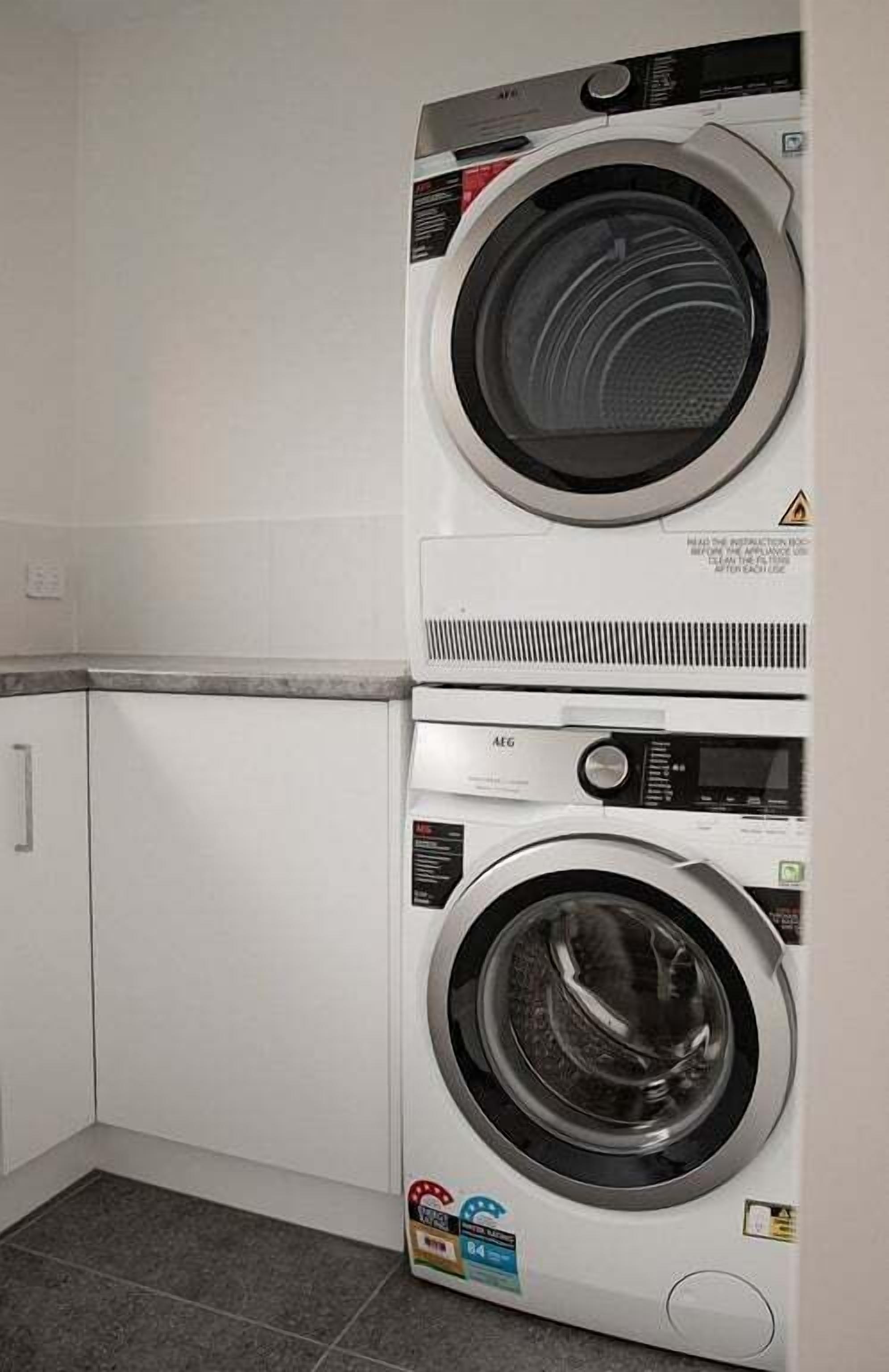 Una lavadora y secadora apiladas en una cocina con gabinetes blancos y salpicadero de azulejos.