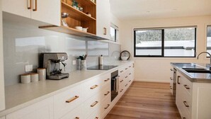 Cocina moderna con armarios blancos, tiradores de madera, horno empotrado y ventana con vistas al exterior.
