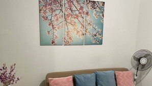 A living room with a brown sofa, a small table with a vase of flowers, and a wall-mounted fan. - Spacious and Cozy Condo near Mall of Asia (Pasay City)
