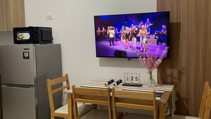 A small kitchen with a refrigerator, microwave, and a TV mounted on the wall displaying a band performing. - Spacious and Cozy Condo near Mall of Asia (Pasay City)
