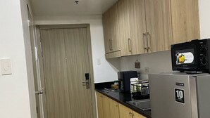 A compact kitchen with wooden cabinets, a stainless steel refrigerator, and a microwave. - Spacious and Cozy Condo near Mall of Asia (Pasay City)