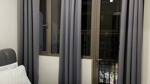 A hotel room with a bed, a window with curtains, an air conditioning unit, and a view of a pharmacy through the window. - Spacious and Cozy Condo near Mall of Asia (Pasay City)