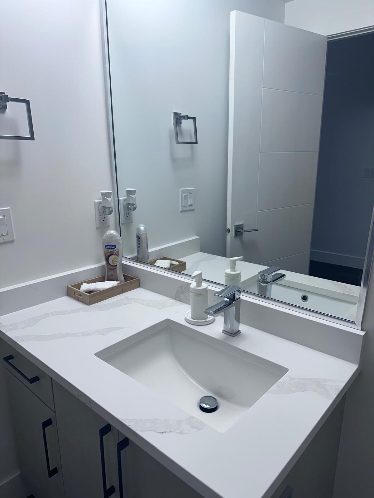 A modern bathroom with a white sink, a large mirror, and a soap dispenser.