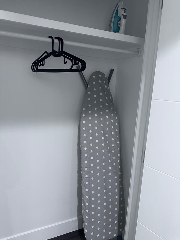 A neatly organized closet with a hanging iron board, a polka-dotted ironing board, and a small shelf with a bottle and a container. - Enjoy a private 2-bedroom basement suite designed for comfort and convenience. (Edmonton)